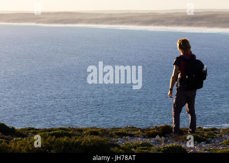 A hiker stops to look at a distant view of a beautiful coastline from a high view point above the sea in southern Australia.