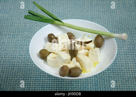 Pieces of white brine cheese and olives were poured over with extra virgin olive oil. Green garlic is lying on the edge of a bowl. Stock Photo