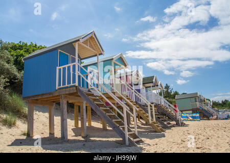 Rows of colourful beach huts on stilts on the sunny, sandy beach at Wells Next The Sea in Norfolk, UK which is a popular tourist beach in England. Stock Photo