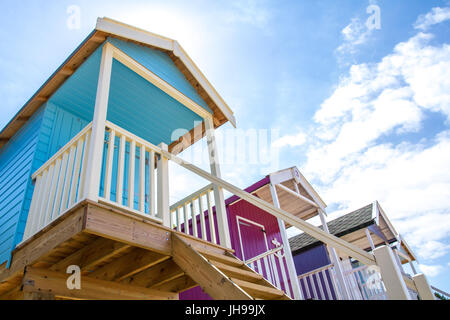 Rows of colourful beach huts on stilts on the sunny, sandy beach at Wells Next The Sea in Norfolk, UK which is a popular tourist beach in England. Stock Photo