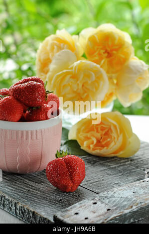 Ripe strawberry in a Cup of pink ceramic on a background of yellow roses. The vertical frame. Stock Photo