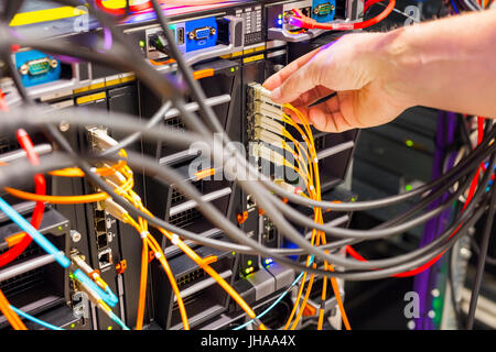Closeup of IT technician's hand plugging fiber channel cable into switch in datacenter Stock Photo
