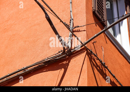 Electrical power cables, telephone cables, and metal water pipes in front of an old building facade Stock Photo