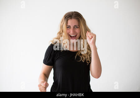 Young, blonde, beautiful, milennial woman expressing excitement and confusion against a white background and in a black shirt indoors during the day. Stock Photo