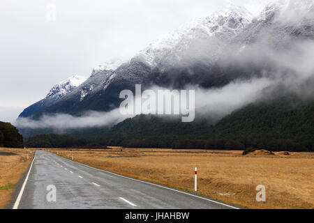 A road disappears into the distance amongst beautiful snow capped mountains. Stock Photo
