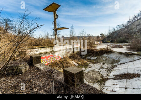 empty old overgrown run-down swimming pool with jumping tower, part of former luxurious site named Barrandov, built by V.M. Havel near city of Prague Stock Photo