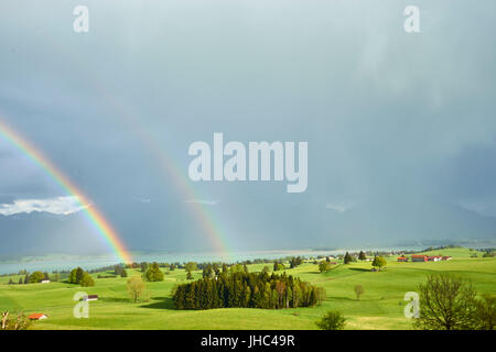 Amazing double rainbow over lush farmlands in the foothills of the Bavarian Alps with Forggensee and Neuschwanstein Castle in the heavy rain Stock Photo