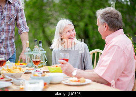 Senior couple enjoying a conversation together at a garden party. They are drinking wine and eating barbecue food. Stock Photo