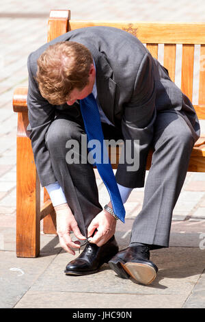 A fashionable well dressed man sitting on a seat bending over tying his right shoe lace in Dundee, UK Stock Photo