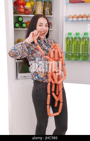 Young girl holds sausages on the refrigerator background. Beautiful young girl near the fridge. Stock Photo