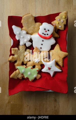 Overhead shot of a variety of plain and iced (frosted) home baked Christmas biscuits (cookies)  in a rectangular white dish with red napkins on wooden Stock Photo