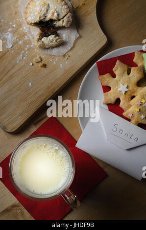 Overhead shot of a Christmas night scene.  A plate of decorated biscuits (cookies), partly eaten mince pie  and glass of milk with envelope addressed  Stock Photo