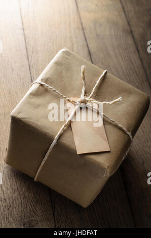 A string tied parcel wrapped in brown paper, with old weathered blank label for copy space.  Set on oak planking to represent table or floor. Stock Photo