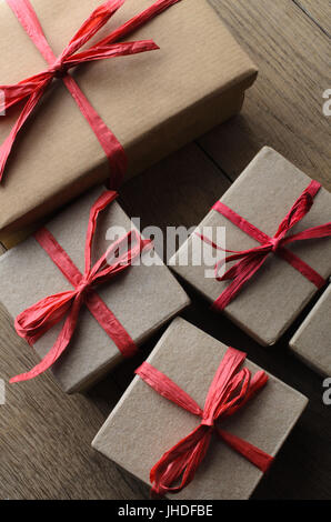 Overhead shot of simple plain brown and paper wrapped gift boxes for Christmas, tied to a bow with red raffia ribbon, on Oak wooden table. Stock Photo