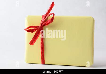 A gift package, very simply wrapped in plain yellow paper with red raffia ribbon tied to a bow.  No label. Copy space on wrapping and background. Stock Photo