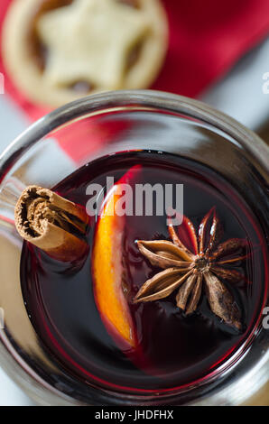 Overhead close up of a glass of spicy mulled wine with star topped Christmas mince pie on red napkin in soft focus background. Stock Photo