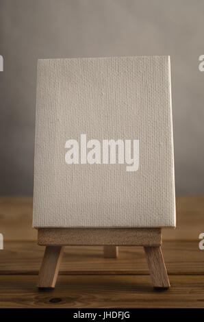 A textured white blank art canvas, in portrait or vertical orientation, resting on an easel on a wood planked floor.  Retro hues. Stock Photo