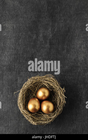 Overhead shot of a nest containing three gold painted eggs on dusty blackboard background with copy space above. Stock Photo