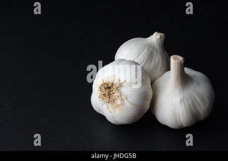 Angled, elevated shot of three whole garlic bulbs on black slate with copy space to the left. Stock Photo