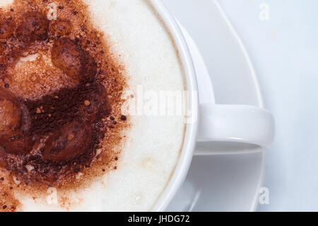 Overhead shot of milk foam and cocoa topping of a latte or cappuccino style coffee in white cup with saucer. Stock Photo