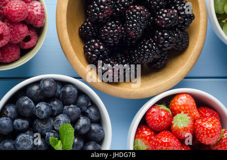 Overhead shot of a variety of fresh, raw fruits in separate bowls on a light blue painted wood plank table. Stock Photo