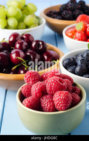 A selection of fresh fruits, separated into a variety of different bowls on a light blue painted wood planked table. Stock Photo