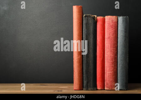 A row of upright books with blank spines at eye level on wood planked desk with black chalkboard background; providing copy space to left. Stock Photo