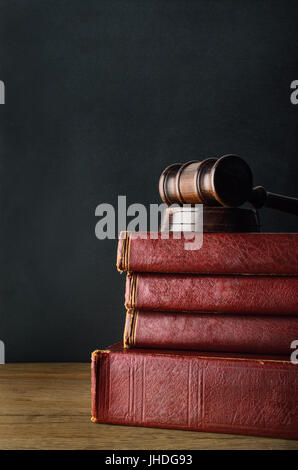 Dark wood gavel on top of a stack of old used books with blank spines, on oak desk with black chalkboard background. Stock Photo