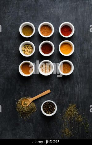 Overhead, flatlay shot of a variety of spices in white bowls with scattered herbs and wooden spoon on dusty blackboard. Stock Photo