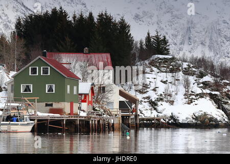 Red-green-white stilt houses with sheet metal roofs and walls in Vestpollen village over Austnesfjorden-Austvagoya island. Fishing boat moored to the  Stock Photo