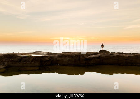 A silhouetted person watches the sunrise over the ocean on a beautiful coastline in Australia.