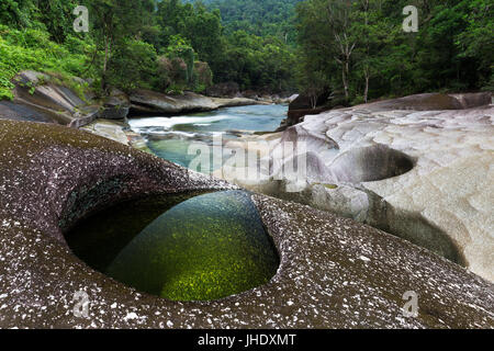 A clear emerald pool in granite rocks beside a river edged by lush tropical rainforest. Stock Photo