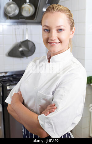 Portrait Of Female Chef Wearing Whites Standing By Cooker In Kitchen Stock Photo