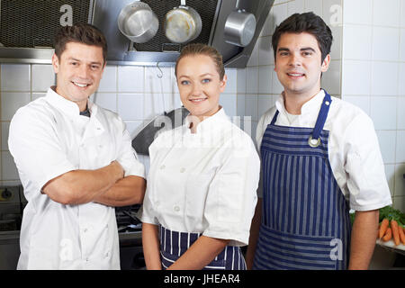 Portrait Of Chef And Staff Standing By Cooker In Kitchen Stock Photo