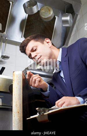 Health Inspector Looking At Oven In Commercial Kitchen Stock Photo