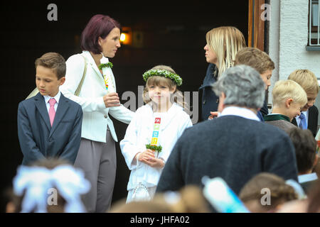 NANDLSTADT, GERMANY - MAY 7, 2017 : A young girl with candle and adults standing in front of church at the first communion in Nandlstadt, Germany. Stock Photo