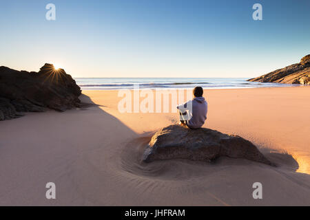 A person sits on a beautiful remote beach in Australia and watches a crisp sunrise over the ocean. Stock Photo