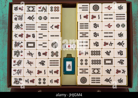Mahjong '麻將' tiles set and box on green wooden background, flat lay Stock Photo