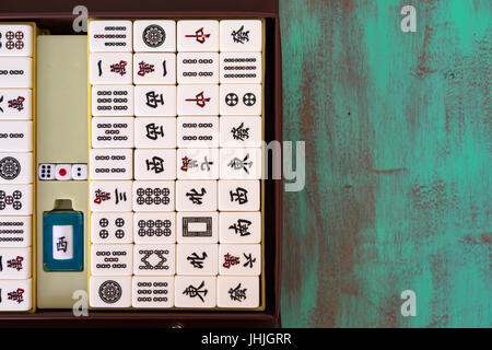 Mahjong '麻將' tiles set and box on green wooden background, flat lay Stock Photo