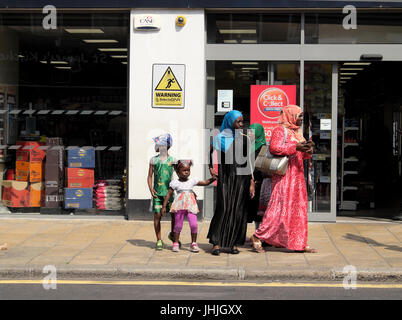 African Muslim family mother daughters, children waiting for a bus outside a store in London UK  KATHY DEWITT Stock Photo