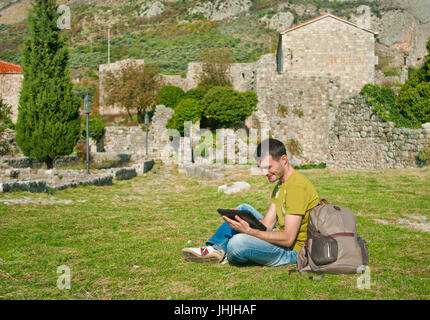 young man using his tablet on grass in Old bar fort, Montenegro Stock Photo