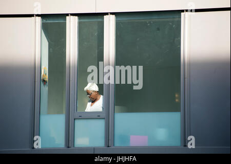 The morning sun shone on a maid, glimpsed through an apartment window in Tribeca, New York City. July 13, 2017 Stock Photo