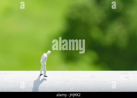 Business and financial  concept. Miniature people : businessman thinking or making decision by walking on high white wall with green nature background Stock Photo
