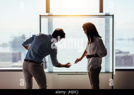 Man and woman entrepreneurs writing business ideas on whiteboard. Business investors discussing business ideas in office. Stock Photo