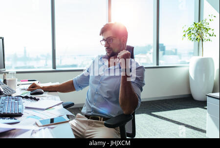 Young entrepreneur looking at the computer screen with concentration at his desk. Businessman in pensive mood sitting at his desk. Stock Photo