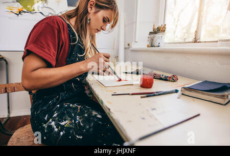 Side view of beautiful female artist drawing pictures in her workshop. Young woman painting in her studio. Stock Photo