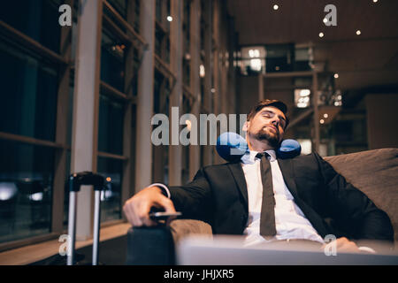 Traveler waiting at airport after flights delays and cancellations. Businessman asleep in airport lounge. Stock Photo