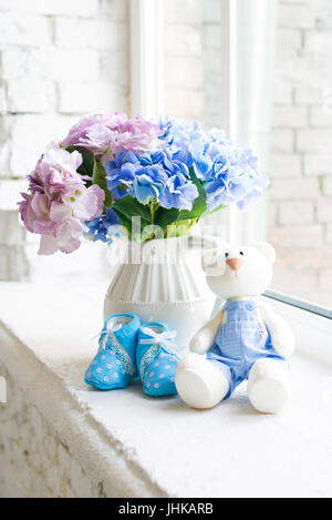 Blue children's shoes with a toy hare and a bouquet of blue flowers on the windowsill Stock Photo