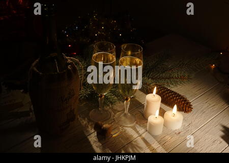Two glasses of champagne, bottle of wine and glowing candles are placed on the table decorated with cones. Stock Photo