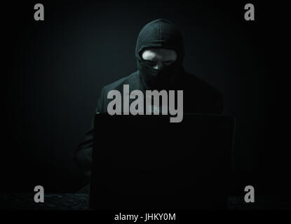 Angry business man as computer hacker in suit stealing data from laptop in front of black background Stock Photo